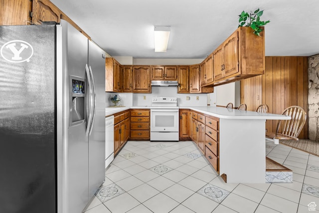 kitchen with white appliances, a peninsula, under cabinet range hood, and light countertops