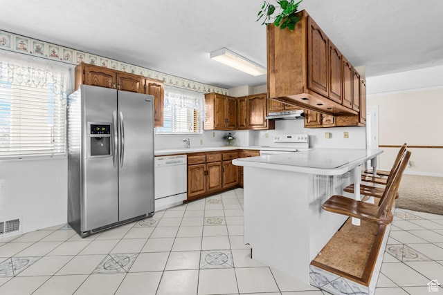 kitchen with visible vents, under cabinet range hood, white appliances, a peninsula, and light countertops