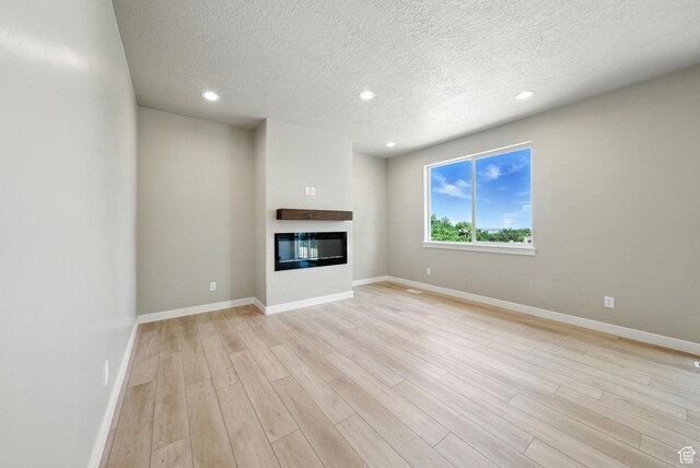 552 E 41st St, South Ogden, UT 84403 - unfurnished living room featuring light wood finished floors, a textured ceiling, a glass covered fireplace, and recessed lighting