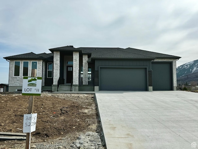 prairie-style home featuring driveway, stone siding, and a garage