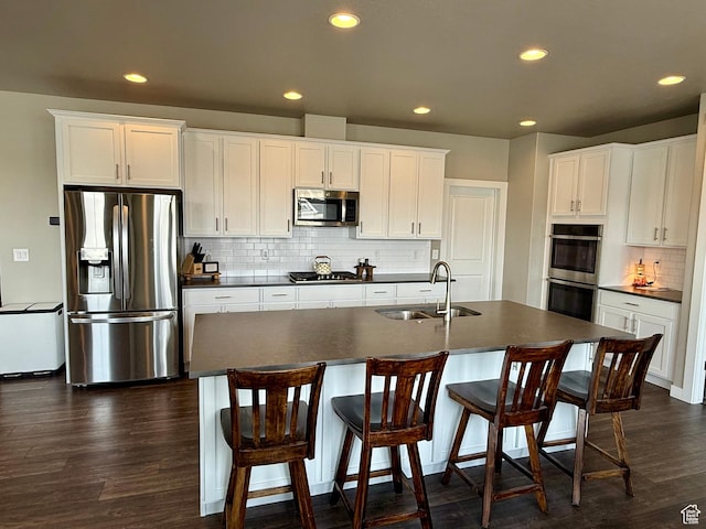 kitchen with dark wood-type flooring, a sink, dark countertops, recessed lighting, and appliances with stainless steel finishes