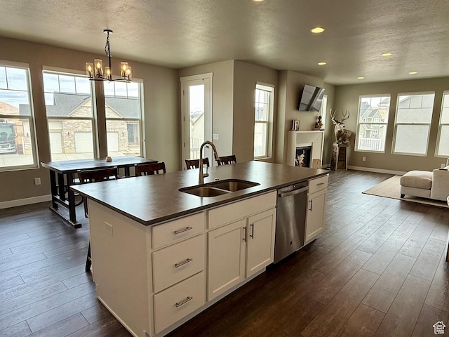 kitchen with a kitchen island with sink, a sink, stainless steel dishwasher, dark countertops, and open floor plan