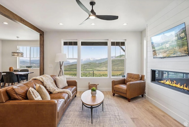 living room featuring a fireplace, light wood-type flooring, ceiling fan, and a wealth of natural light