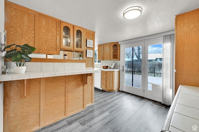 kitchen featuring glass insert cabinets, tile countertops, visible vents, and light wood-type flooring