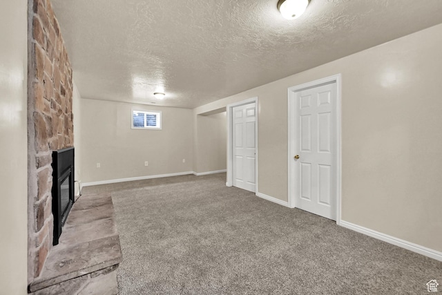 basement featuring a textured ceiling, a fireplace, baseboards, and carpet
