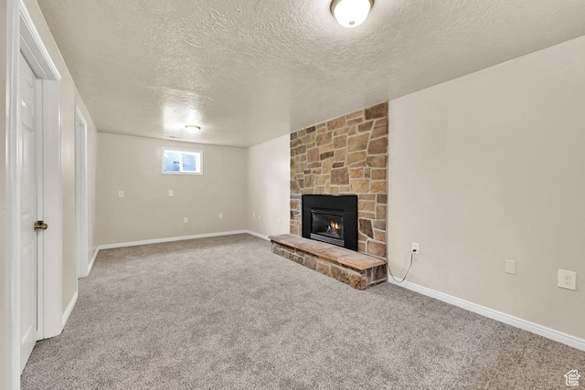 unfurnished living room featuring a stone fireplace, carpet, baseboards, and a textured ceiling