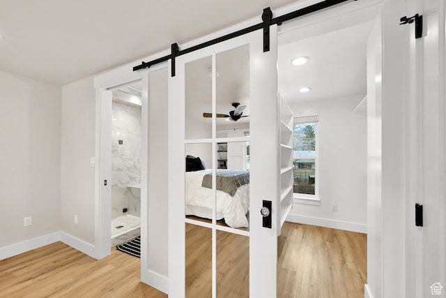 bedroom with baseboards, a barn door, wood finished floors, and ensuite bath