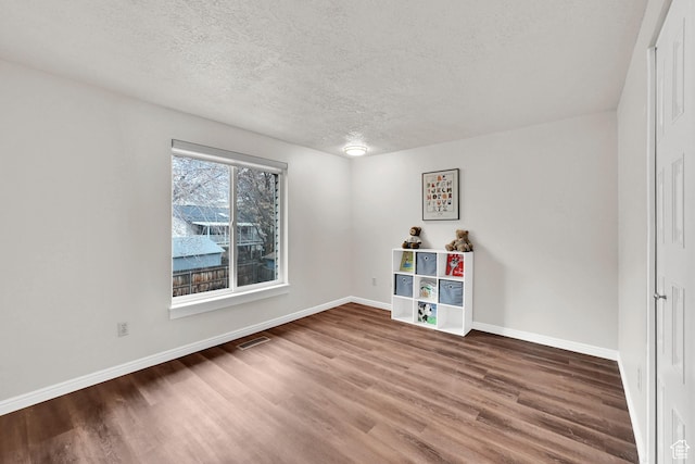 empty room featuring baseboards, visible vents, a textured ceiling, and wood finished floors