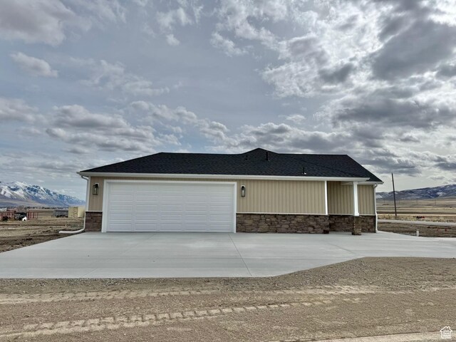 18136 N 6000 W, Garland, UT 84312 - view of front facade with stone siding, a mountain view, driveway, and an attached garage