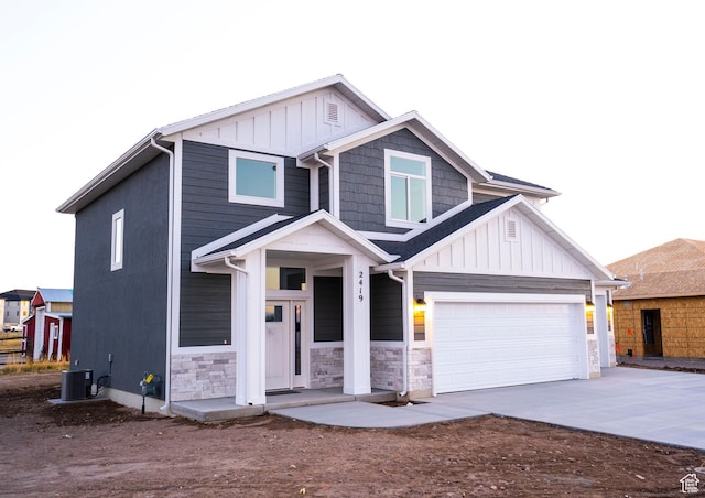 view of front facade with concrete driveway, stone siding, board and batten siding, and central AC