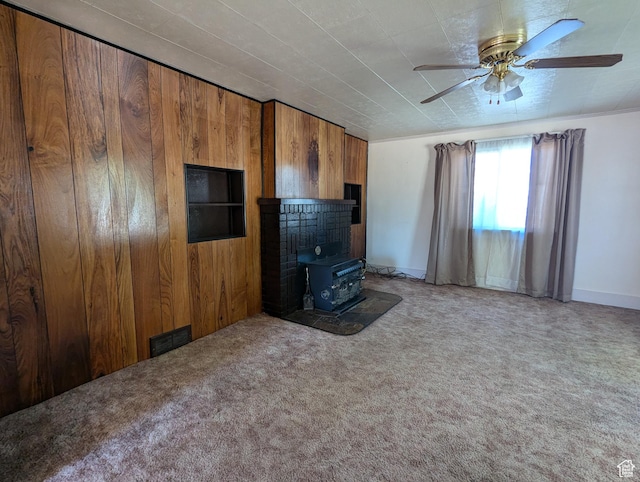 unfurnished living room featuring visible vents, carpet, wood walls, ceiling fan, and a wood stove