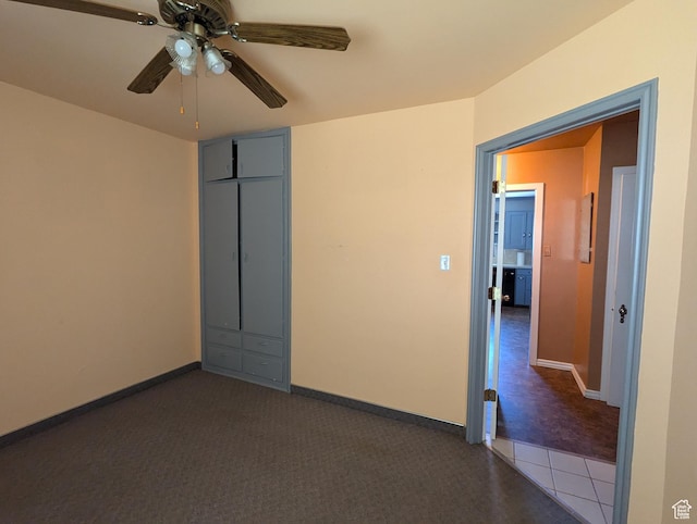 unfurnished room with a ceiling fan, baseboards, and dark colored carpet