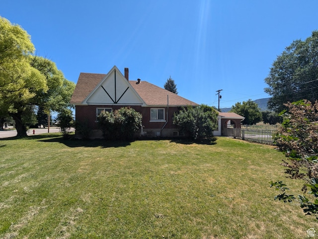 rear view of property featuring a shingled roof, a chimney, a yard, and fence