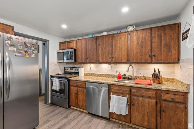 kitchen featuring light wood-style flooring, a sink, light stone counters, tasteful backsplash, and appliances with stainless steel finishes