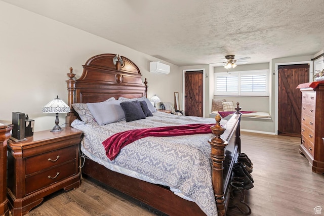 bedroom with an AC wall unit, wood finished floors, baseboards, and a textured ceiling