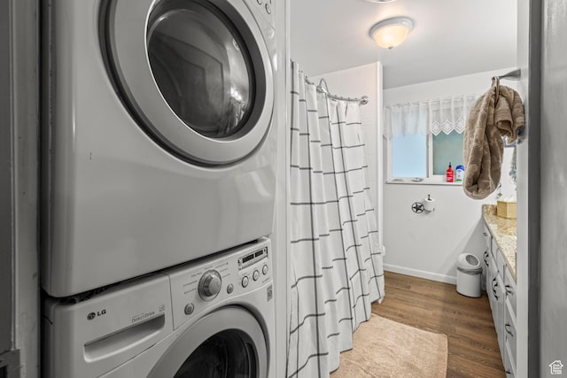 washroom with laundry area, stacked washer and dryer, wood finished floors, and baseboards