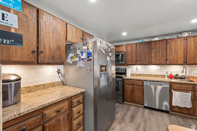 kitchen featuring a sink, light wood-type flooring, tasteful backsplash, and appliances with stainless steel finishes