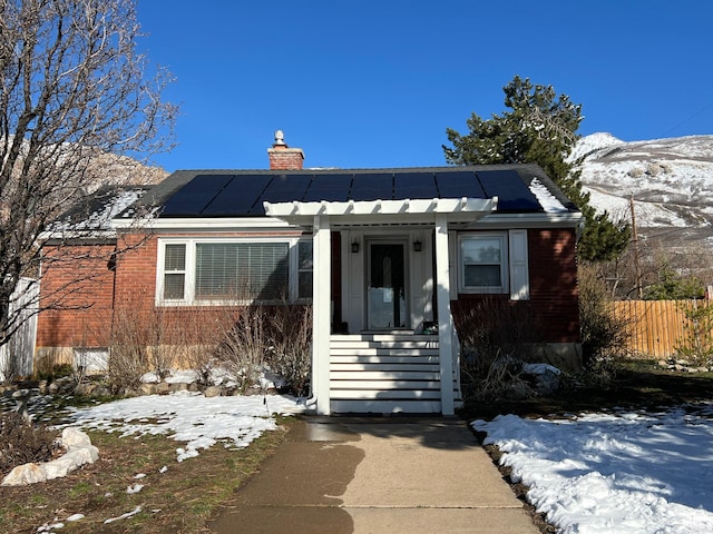 bungalow-style home with roof mounted solar panels, a chimney, and fence