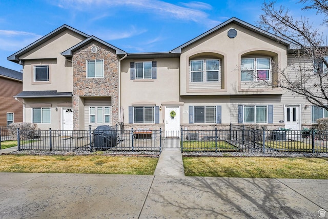 multi unit property featuring stone siding, a fenced front yard, and stucco siding