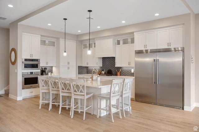 5401 S Aquamarine Ln E, St George, UT 84790 - kitchen featuring tasteful backsplash, light countertops, an island with sink, light wood-style flooring, and stainless steel appliances