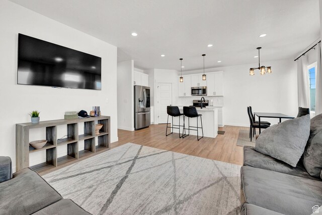 living area featuring recessed lighting, baseboards, light wood-style floors, and an inviting chandelier