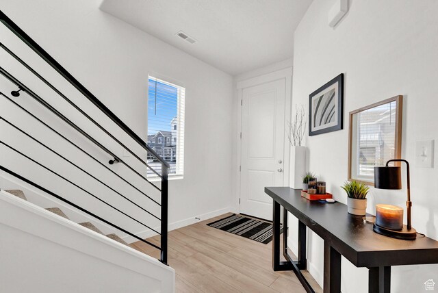 foyer featuring light wood finished floors, stairway, baseboards, and visible vents