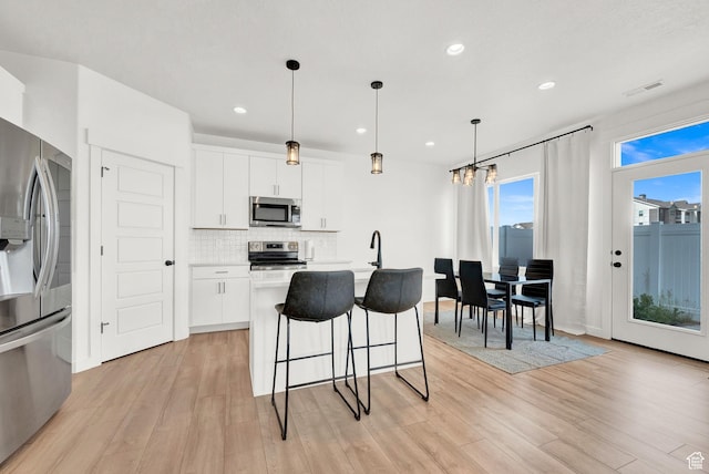 kitchen with a breakfast bar, decorative backsplash, light countertops, appliances with stainless steel finishes, and light wood-type flooring