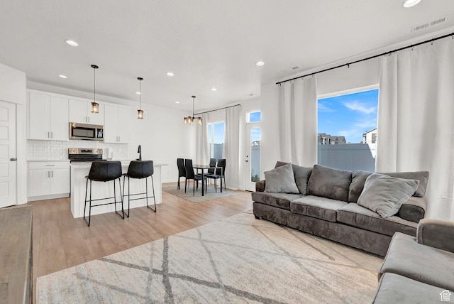 living area with a notable chandelier, light wood-style floors, recessed lighting, and a healthy amount of sunlight