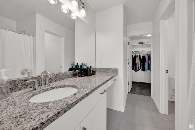 bathroom featuring a spacious closet, tile patterned flooring, baseboards, toilet, and vanity