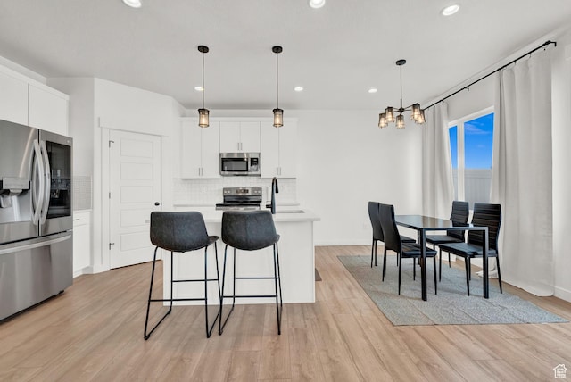 kitchen featuring light wood-type flooring, backsplash, appliances with stainless steel finishes, light countertops, and a chandelier