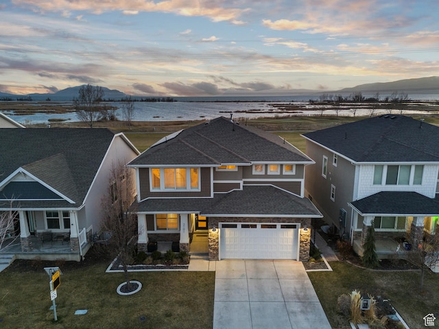 view of front of property with a front lawn, driveway, stone siding, a shingled roof, and a water and mountain view