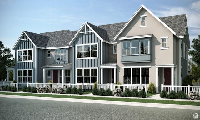 view of front facade with fence, covered porch, board and batten siding, and a shingled roof