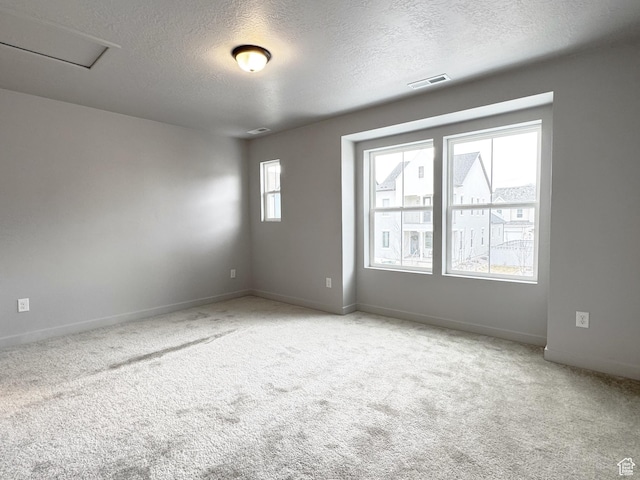 carpeted spare room with baseboards, visible vents, and a textured ceiling