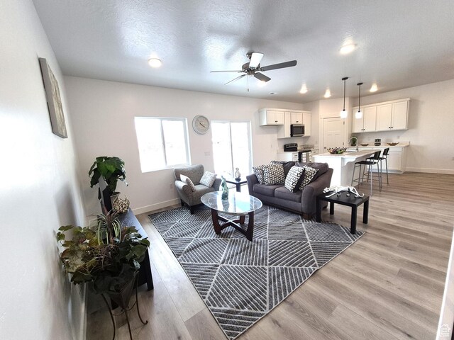 living area with ceiling fan, a textured ceiling, baseboards, and light wood-style floors