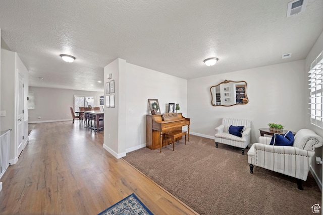 sitting room with visible vents, wood finished floors, baseboards, and a textured ceiling