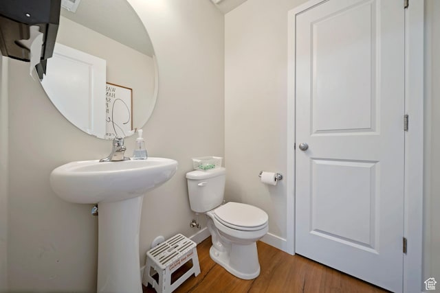 half bath with baseboards, toilet, and wood finished floors