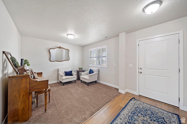 sitting room with visible vents, baseboards, a textured ceiling, and wood finished floors