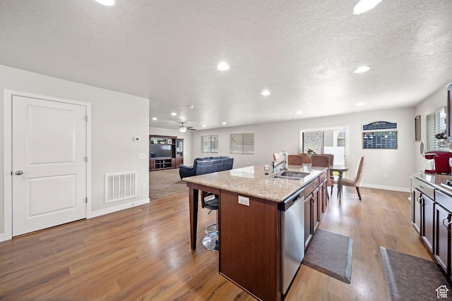kitchen with visible vents, light wood-style flooring, a sink, a kitchen breakfast bar, and dishwasher