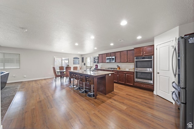 kitchen featuring a kitchen island with sink, a kitchen bar, appliances with stainless steel finishes, and wood finished floors