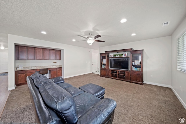 living area with baseboards, visible vents, ceiling fan, a textured ceiling, and dark carpet