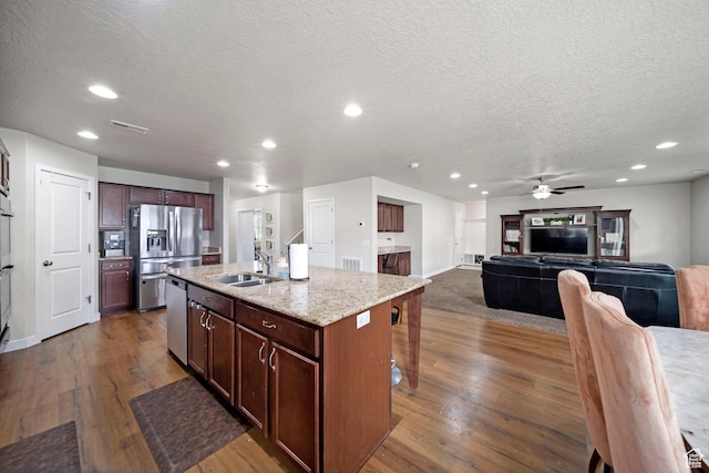 kitchen featuring dark wood-type flooring, an island with sink, appliances with stainless steel finishes, and a sink