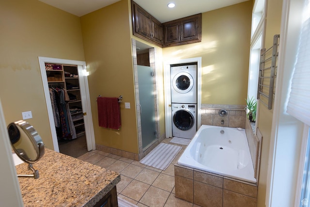 full bathroom with stacked washing maching and dryer, a whirlpool tub, tile patterned flooring, a shower stall, and a walk in closet