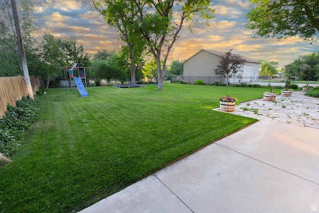 yard at dusk with a playground, a patio area, a fenced backyard, and an outdoor fire pit