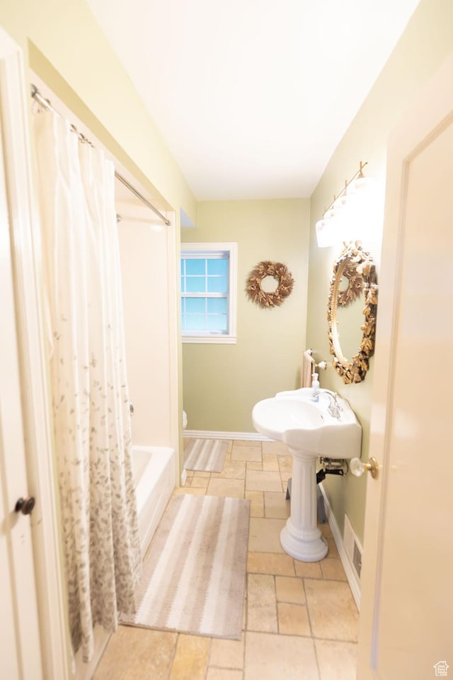 bathroom featuring visible vents, baseboards, shower / tub combo with curtain, and stone tile flooring