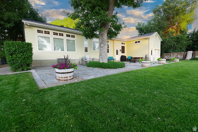 rear view of house with a yard, fence, stucco siding, and a patio area
