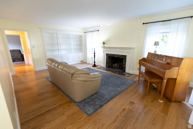 living room featuring built in shelves, crown molding, baseboards, a fireplace, and wood finished floors