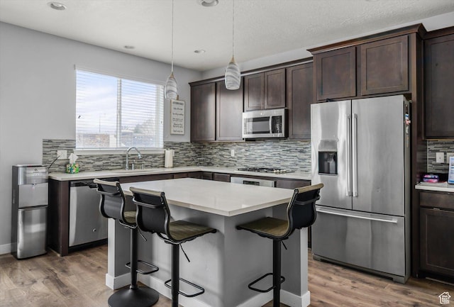 12172 S Window Arch Ln, Herriman, UT 84096 - kitchen with a center island, a sink, light wood-style floors, dark brown cabinetry, and appliances with stainless steel finishes