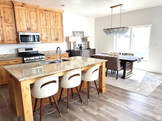 352 W Ropelato Dr, Nibley, UT 84321 - kitchen featuring stainless steel appliances, a sink, light wood-type flooring, a kitchen bar, and light stone countertops