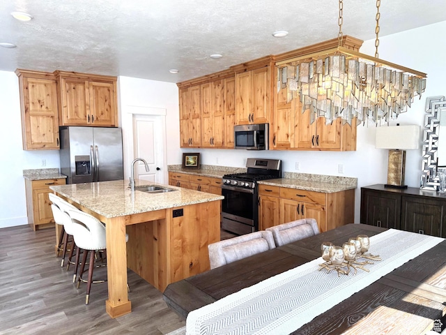 352 W Ropelato Dr, Nibley, UT 84321 - kitchen with stainless steel appliances, a sink, a kitchen bar, wood finished floors, and a center island with sink
