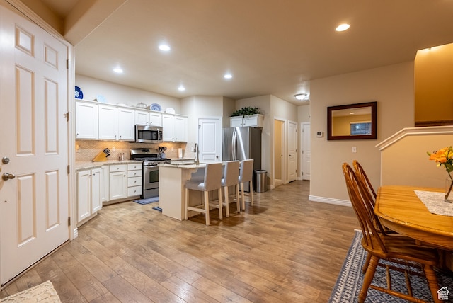160 S 2775 W, West Point, UT 84015 - kitchen featuring light wood finished floors, decorative backsplash, appliances with stainless steel finishes, white cabinetry, and a kitchen breakfast bar